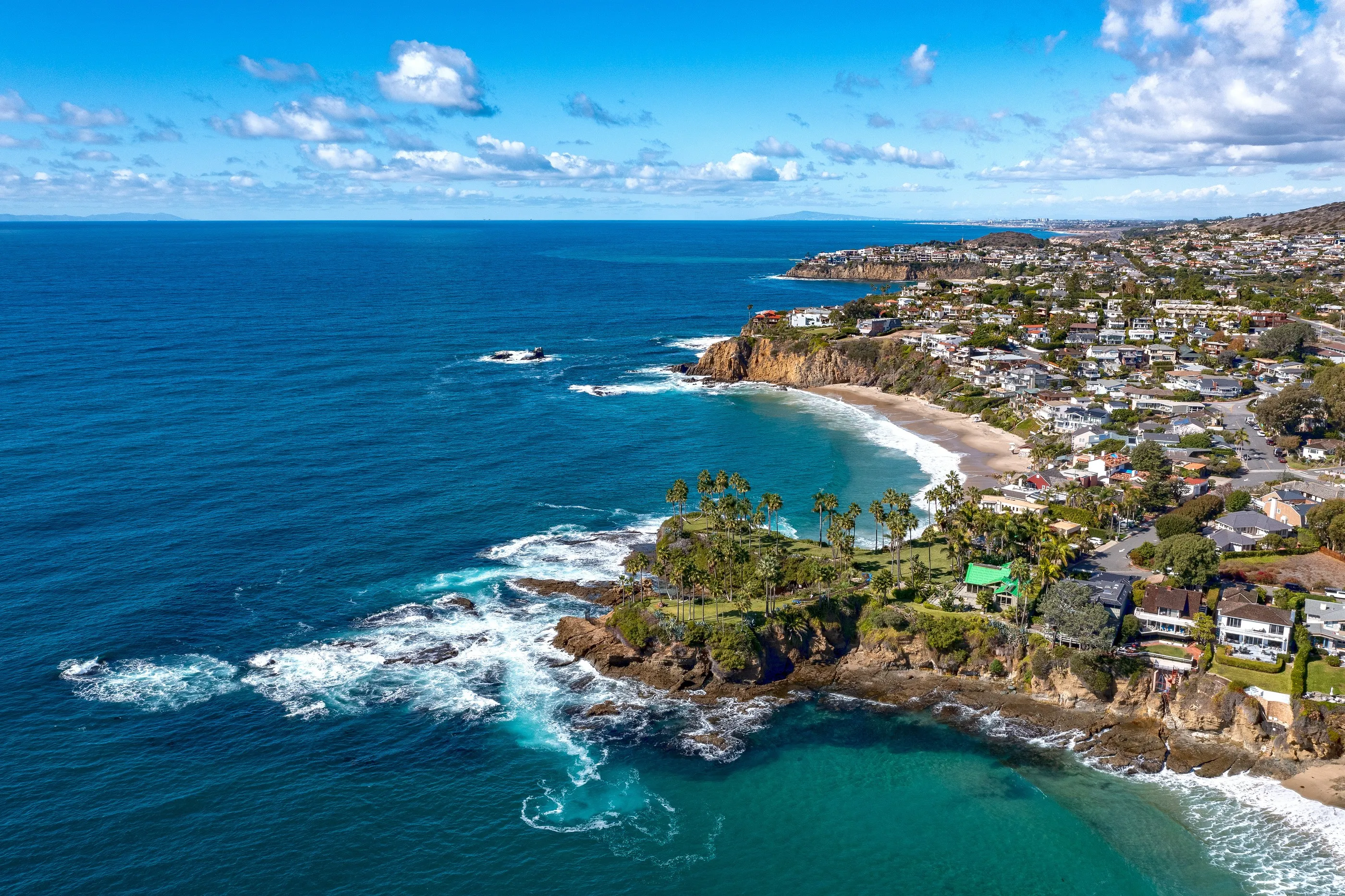 Aerial view of the Orange County coastline, with cliffs, a cove, and coastal homes above the water