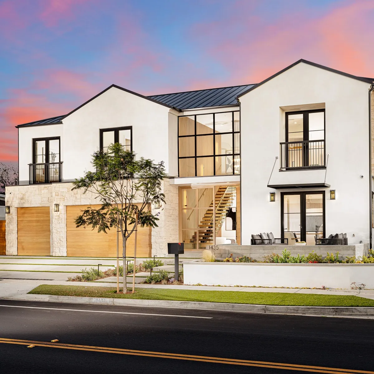 Modern farmhouse at dusk with a lit interior and a pink sky